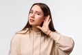 Young pretty brunette woman keeps palm of a hand close to ear as if listening to rumors isolated over white background Royalty Free Stock Photo