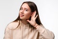 Young pretty brunette woman keeps palm of a hand close to ear as if listening to rumors isolated over white background Royalty Free Stock Photo