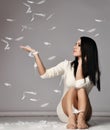 Young pretty brunette woman in mini dress sitting on floor and catching white feathers meaning softness after laser hair Royalty Free Stock Photo