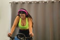 Young, pretty, brunette woman, pink headphones, wearing yellow top and black leggings, spinning on a bike at the gym. Fitness Royalty Free Stock Photo