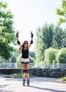 Young pretty brunette woman, riding rollerblades in city park with green trees. Fit sporty girl, wearing black top and white Royalty Free Stock Photo