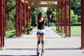 Young pretty brunette woman, riding rollerblades in city park with green trees. Fit sporty girl, wearing black top and white Royalty Free Stock Photo