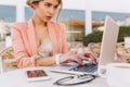 Young pretty business woman working on laptop in street cafe, typing on keyboard, smart lady seriously looking on screen