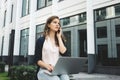 Young pretty businesswoman sits in urban street and discussing about work on smartphone and search information in internet