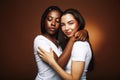 Young pretty caucasian, afro woman posing cheerful together on brown background, lifestyle diverse nationality people