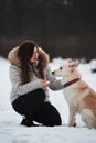 Spend holidays with dog in nature. Young pretty Caucasian girl with long hair is sitting in winter park with her friend white