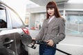 Young pretty Caucasian red haired woman in trendy casual outfit, refilling petrol in her luxury modern car at self Royalty Free Stock Photo