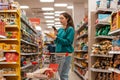 A young pretty Caucasian woman scans the qr code on a food package using her smartphone. In the background is a supermarket. Royalty Free Stock Photo