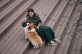 A young pretty Caucasian woman is sitting on the steps in the city center with her little red shepherd dog. Welsh corgi Royalty Free Stock Photo