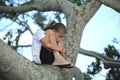 Young pretty child girl sitting relaxed between big branches of old tree on sunny summer day Royalty Free Stock Photo