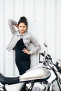 Young pretty cute brunette girl dressed in a little black dress and a jacket standing near a motorcycle Royalty Free Stock Photo