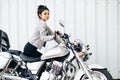 Young pretty cute brunette girl dressed in a little black dress and a jacket standing near a motorcycle Royalty Free Stock Photo