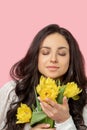 Young pretty dark-haired woman holding yellow flowers and smelling them