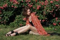 Young pretty fashion model sits in the rose garden. Outdoor portrait of a romantic girl with hard sunlight