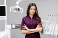 A young pretty female dentist is standing by the dental chair in the office with her arms crossed in front of her Royalty Free Stock Photo