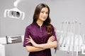 A young pretty female dentist is standing by the dental chair in the office with her arms crossed in front of her Royalty Free Stock Photo