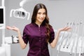 A young pretty female dentist is standing near the dental chair in the office, gesturing with her hands Royalty Free Stock Photo