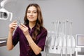 A young pretty female dentist is standing near the dental chair in the office, holding tools for work and looking into the camera Royalty Free Stock Photo