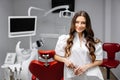 A young pretty female dentist is standing near the dental chair in the office, holding tools for work and looking into the camera Royalty Free Stock Photo