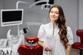 A young pretty female dentist is standing near the dental chair in the office, holding tools for work and looking into the camera Royalty Free Stock Photo