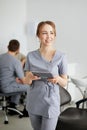 A young pretty female dentist stands in the middle of the office, and in the background a colleague is advising patients Royalty Free Stock Photo