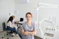 A young pretty female dentist stands in the middle of the office, and in the background a colleague is advising patients Royalty Free Stock Photo