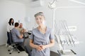 A young pretty female dentist stands in the middle of the office, and in the background a colleague is advising patients Royalty Free Stock Photo