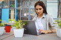 Beautiful entrepreneur using laptop during lunch in outdoor cafe, elegant businesswoman holding coffee cup working in city street. Royalty Free Stock Photo