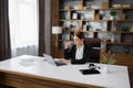 Young pretty female freelancer in business suit with pen in her hand, sitting at table with laptop Royalty Free Stock Photo