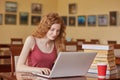 Young pretty female student with laptop and books working in high school library, sitting at table, takeaway cooffe near her books Royalty Free Stock Photo