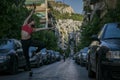 A young pretty fitness female dancer is posing on the city narrow street in the summer evening in front of the high hill