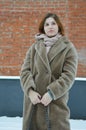 A young pretty girl in a beige fur coat without a hat stands near a brick wall Royalty Free Stock Photo