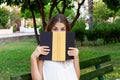 Young pretty girl is covering her face with a book because of feeling surprise and shock. Emotional funny woman is holding a book