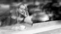 A young pretty girl with a cup of coffee in a cafe in front of the window. View from outside through glass with reflections. Black