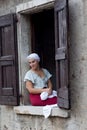 Young pretty girl in medieval costume, dressed like a washerwoman, sitting at the window looking down gently and smiling