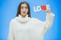 Young pretty girl dressed in white clothes. During this time it stands on a blue background. Holds a word of love in