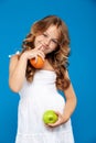 Young pretty girl holding apple and orange over blue background. Royalty Free Stock Photo