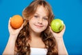 Young pretty girl holding apple and orange over blue background. Royalty Free Stock Photo