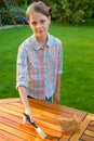 Young pretty girl holding a brush applying varnish paint on a wooden garden table Royalty Free Stock Photo