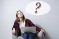 Young girl with a laptop sitting on a soft comfortable chair and thinking, a woman using a computer against a white blank wall, Royalty Free Stock Photo