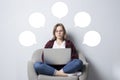 Young girl with a laptop sitting on a soft comfortable chair and thinking, a woman using a computer against a white blank wall, Royalty Free Stock Photo