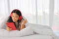 Young pretty girl listening to music from home while lying down on her bed using tablet to access media online Royalty Free Stock Photo