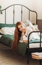 A young pretty girl with long hair lies on a bed in the bedroom. Day rest and relaxation. Vertical photo Royalty Free Stock Photo