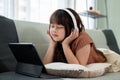 Young pretty girl is lying on a sofa and enjoying listening to music on her headphones Royalty Free Stock Photo