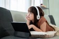 Young pretty girl is lying on a sofa and enjoying listening to music on her headphones Royalty Free Stock Photo