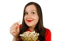 Young pretty girl with opened mouth and wide eyes holds glass bowl with popcorn isolated on white background