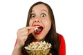 Young pretty girl with opened mouth and wide eyes holds glass bowl with popcorn isolated on white background