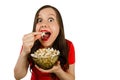 Young pretty girl with opened mouth and wide eyes holds glass bowl with popcorn isolated on white background