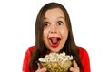 Young pretty girl with opened mouth and wide eyes holds glass bowl with popcorn isolated on white background