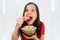 Young pretty girl with opened mouth and wide eyes holds glass bowl with popcorn